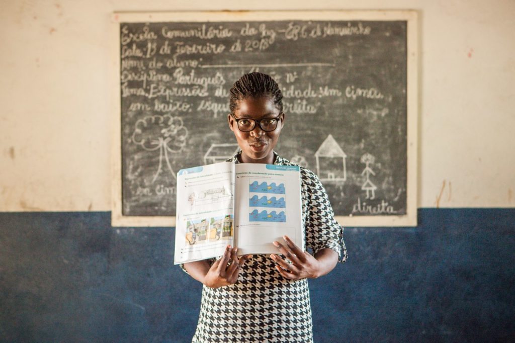 A teacher from Peace school in Mozambique standing with an open book in front of the classroom 