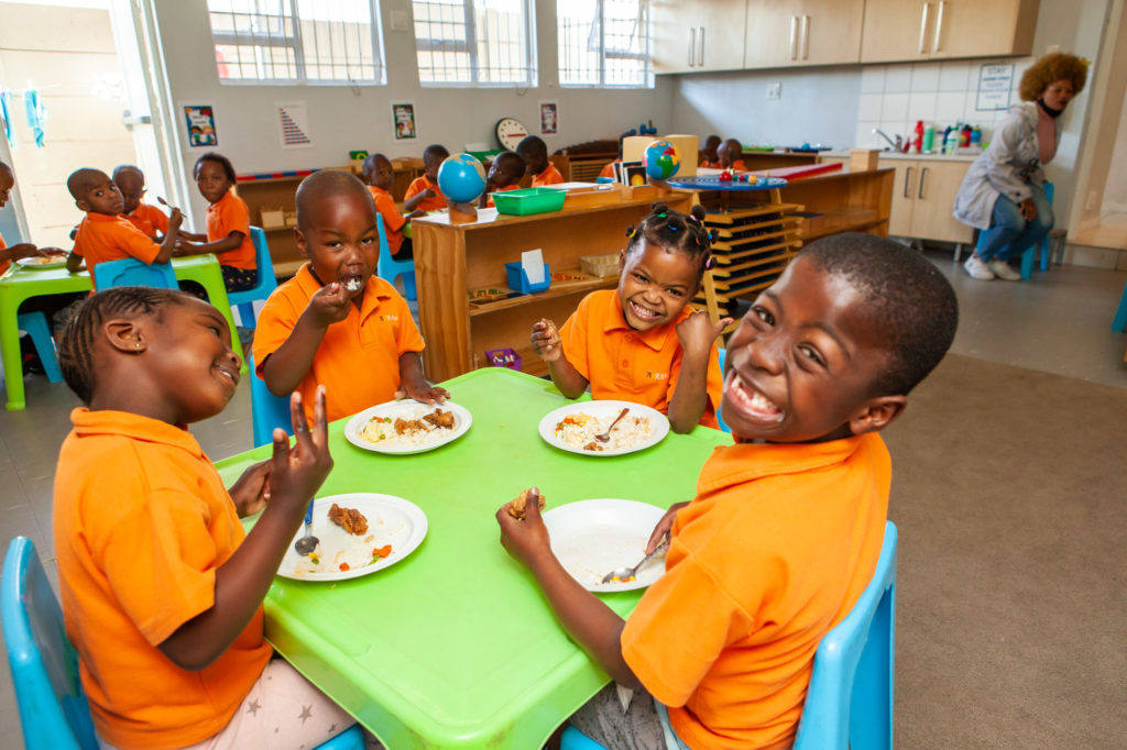 Ndinawe smiling while sitting at the table and having lunch with his friends 